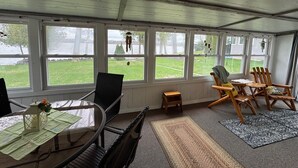 A covered patio with a table, chairs, and a view of a grassy area and lake. - Just Peachy! Enjoy your private lake front home. (West Branch)