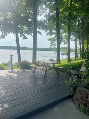 A wooden deck with a picnic table and chairs, overlooking a lake with boats.