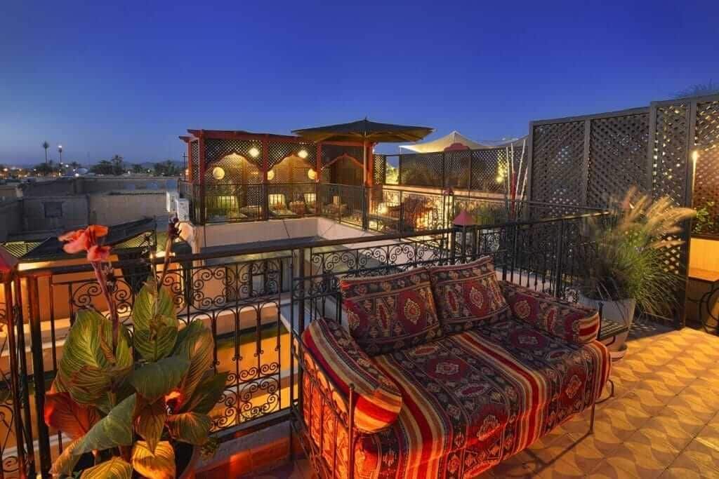 Een terras met een gestreept bankje, een overdekte zithoek en een decoratieve omheining.