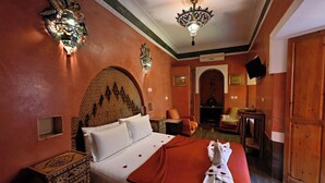 A hotel room with a bed, a decorative wall, a television, and a wooden door. - Riad La Maison Nomade (Marrakech)
