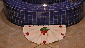 A circular blue-tiled bathtub with a candle on it, surrounded by a beige tiled floor with a decorative white fan with red flowers. - Riad La Maison Nomade (Marrakech)