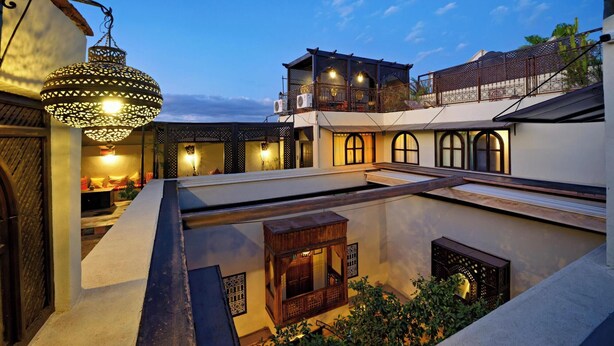 A courtyard with a hanging lantern, a wooden bench, and a building with a balcony. - Riad La Maison Nomade (Marrakech)