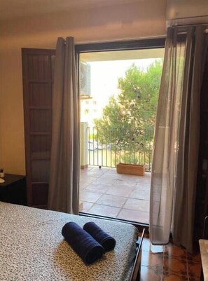 Een hotelkamer met een bed, een klein tafeltje en uitzicht op een balkon met een hekwerk en groen.