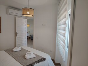 Ein Hotelzimmer mit einem Bett, einer Hängelampe, einer Tür zu einem anderen Raum und einem Fenster mit Jalousien.