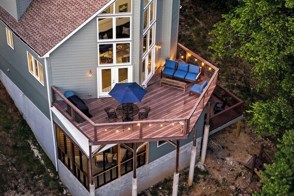 Una casa de dos pisos con terraza, ventanas amplias y mobiliario exterior.