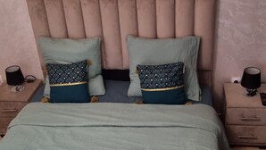 Una cama con cabecera, dos almohadas, una colcha y dos toallas enrolladas.