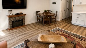 Ein Wohnzimmer mit Kamin, Fernseher, Essbereich mit Stühlen und einer Küche mit Schränken.