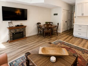 Ein Wohnzimmer mit Kamin, Fernseher, Essbereich mit Stühlen und einer Küche mit Schränken.