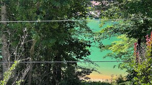 Ein gepflasterter Weg führt zu einem von einer Mauer umgebenen Bereich mit dichter Vegetation und Blick auf ein grünes Gewässer.