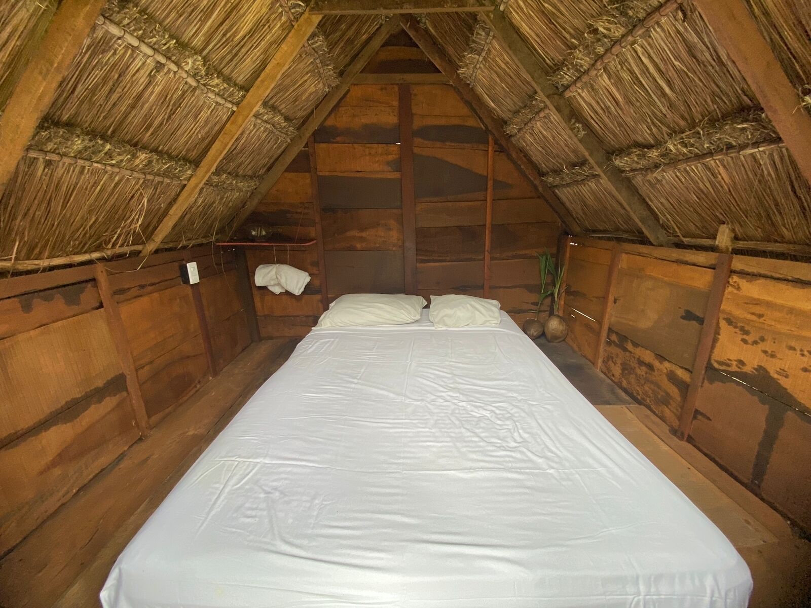 Una cama individual en una habitación de madera en el ático, con techo de paja.