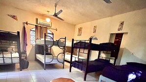 A room with bunk beds, a ceiling fan, a small wooden stool, and a patterned rug.