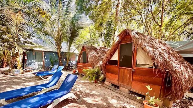 A row of thatched-roof huts with blue lounge chairs in front. - Hostalito Lahar (Bacalar)
