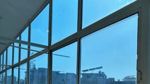 Un pasillo con ventanas amplias, piso de baldosas y vista de edificios al exterior.