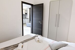 Quarto de hotel com cama, guarda-roupa e porta aberta para uma cozinha compacta.