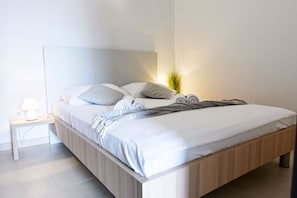 A modern bedroom with a wooden bed frame, white bedding, and a bedside lamp. - Family Friendly Stay With Pool and Game Room (Tar-Vabriga)