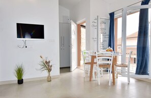 Een moderne keuken met een televisie, een eettafel met stoelen, een potplant en een raam met gordijnen.