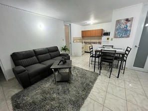 Ein Wohnzimmer mit schwarzem Sofa, Couchtisch und Essbereich mit Tisch und Stühlen.