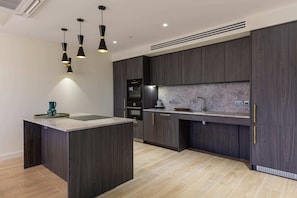 Une cuisine moderne avec des meubles de couleur bois foncé, un îlot central et des luminaires suspendus.