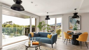Uma sala de estar moderna com um sofá azul, cadeiras amarelas, uma mesa de centro redonda e uma área de jantar com mesa e cadeiras pretas.