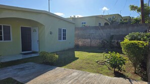 A residential property with a paved driveway, a small lawn, and a stone wall. - Sun-Filled Cozy House Near Beautiful Beach (Discovery Bay, St. Ann)