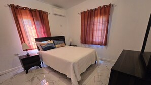 A bedroom with a bed, nightstands, a dresser, and curtains. - Sun-Filled Cozy House Near Beautiful Beach (Discovery Bay, St. Ann)