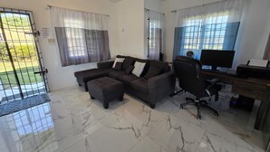 A modern living room with a sectional sofa, a desk with a computer, and a chair. - Sun-Filled Cozy House Near Beautiful Beach (Discovery Bay, St. Ann)