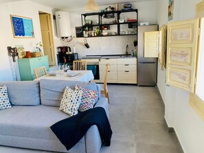 Una cocina moderna con horno empotrado, un comedor con mesa lista para usar y una sala de estar con sofá y cojines decorativos.