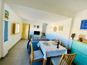 Un área de comedor con una mesa preparada para cuatro personas, un sofá, un televisor y una escalera al fondo.