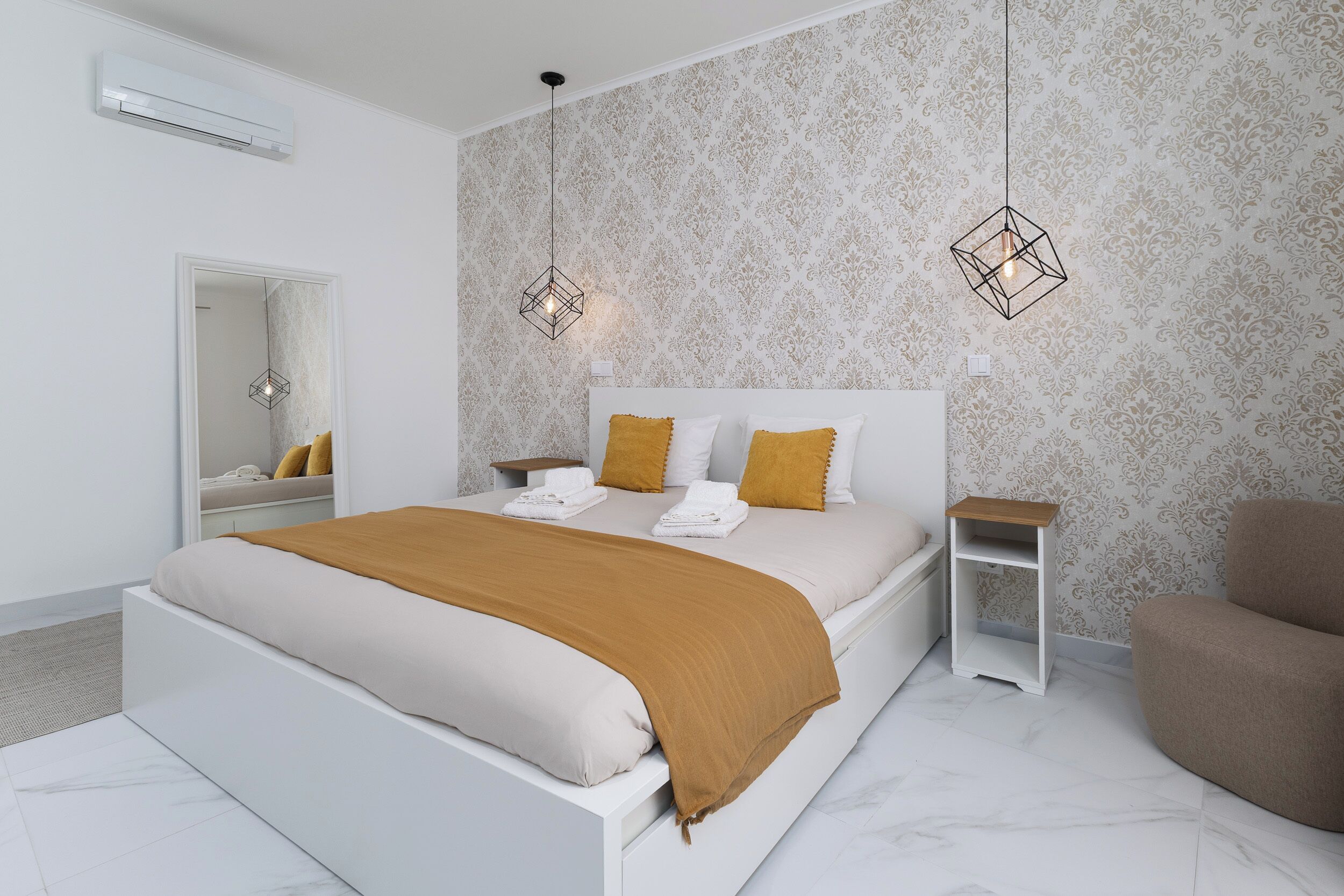 Un dormitorio moderno con cama, mesitas de noche, una silla y papel tapiz estampado.
