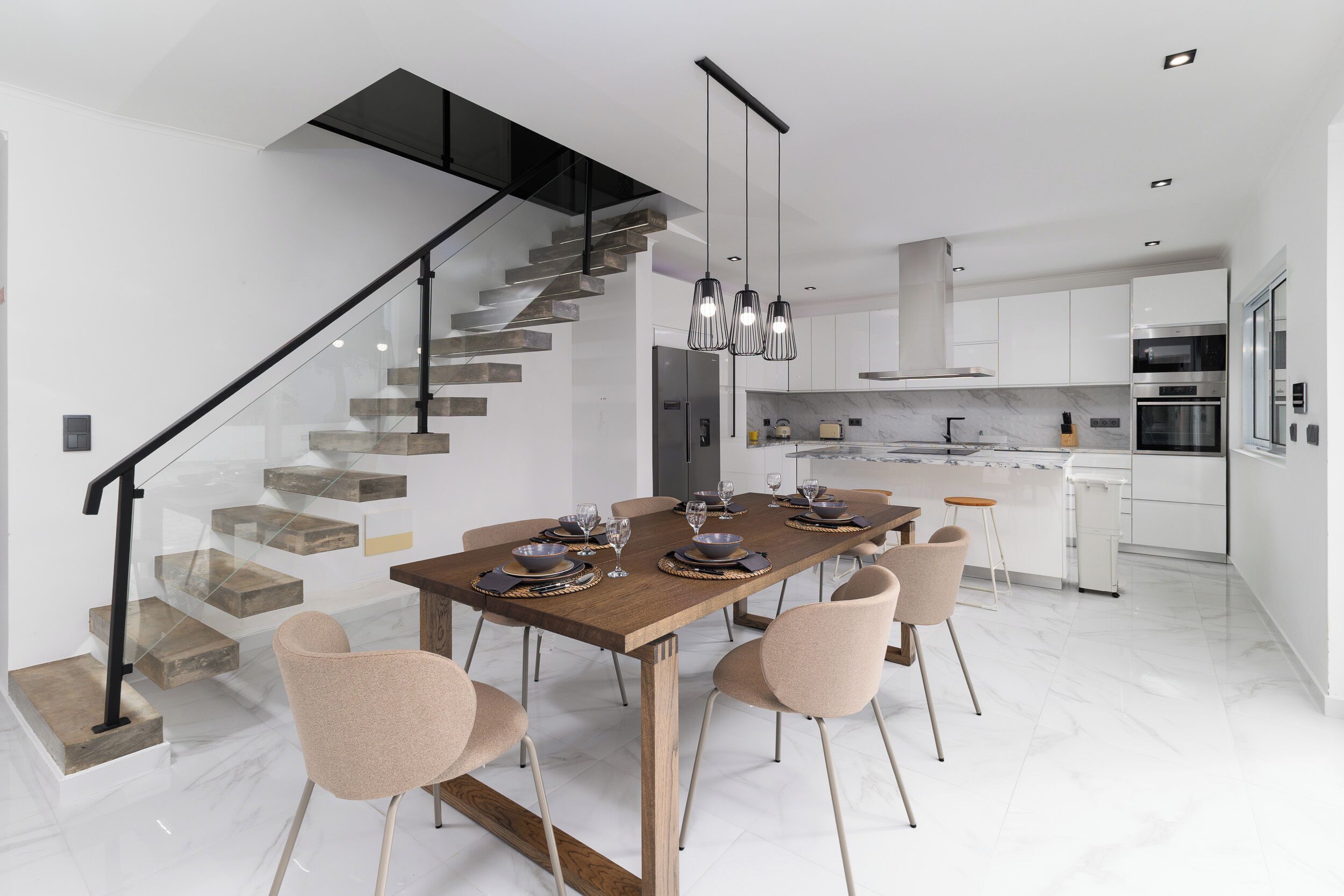 A modern kitchen with white cabinets, stainless steel appliances, and a wooden dining table set for six.