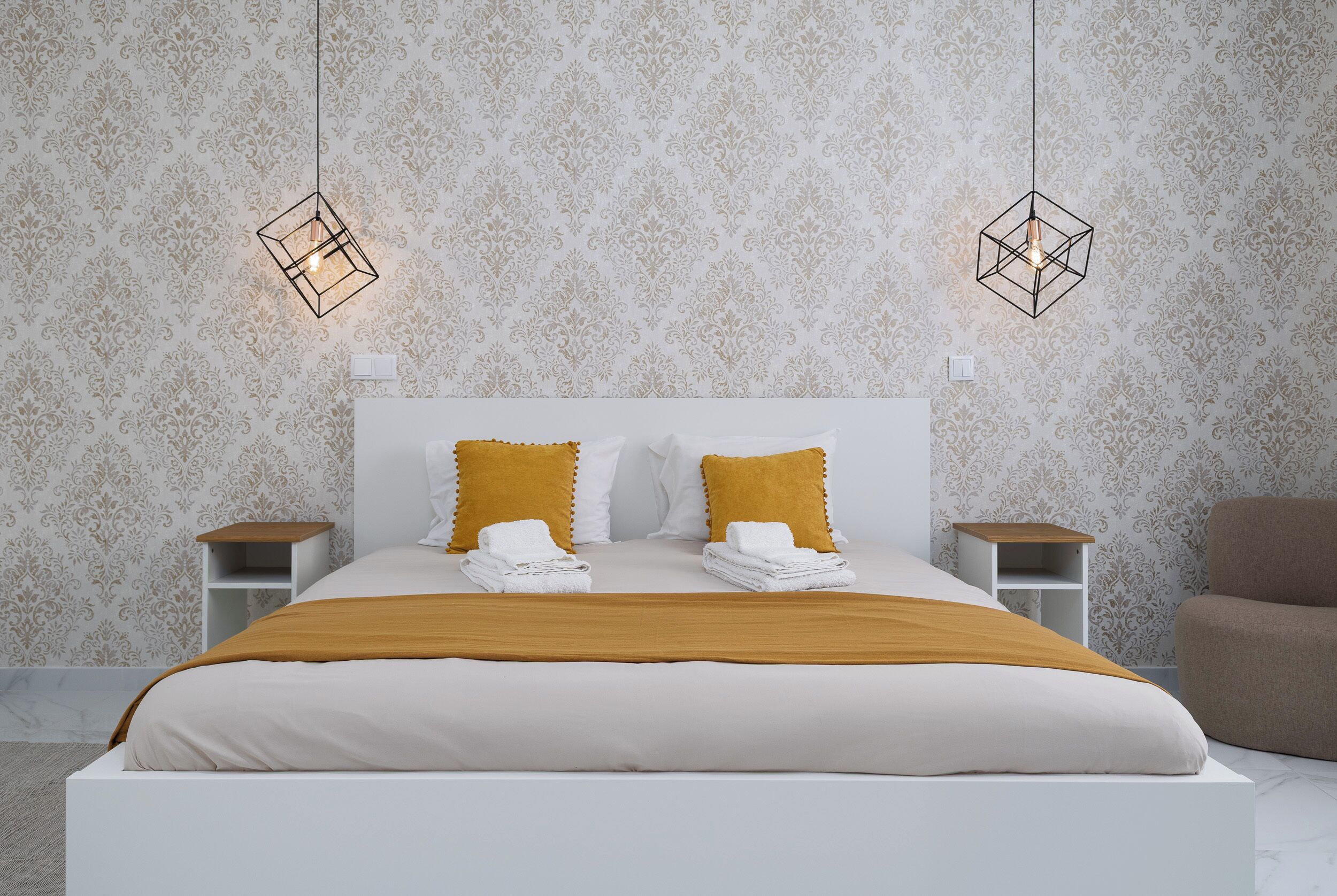 A neatly made bed with white and mustard pillows, two bedside tables, and a hanging light fixture.