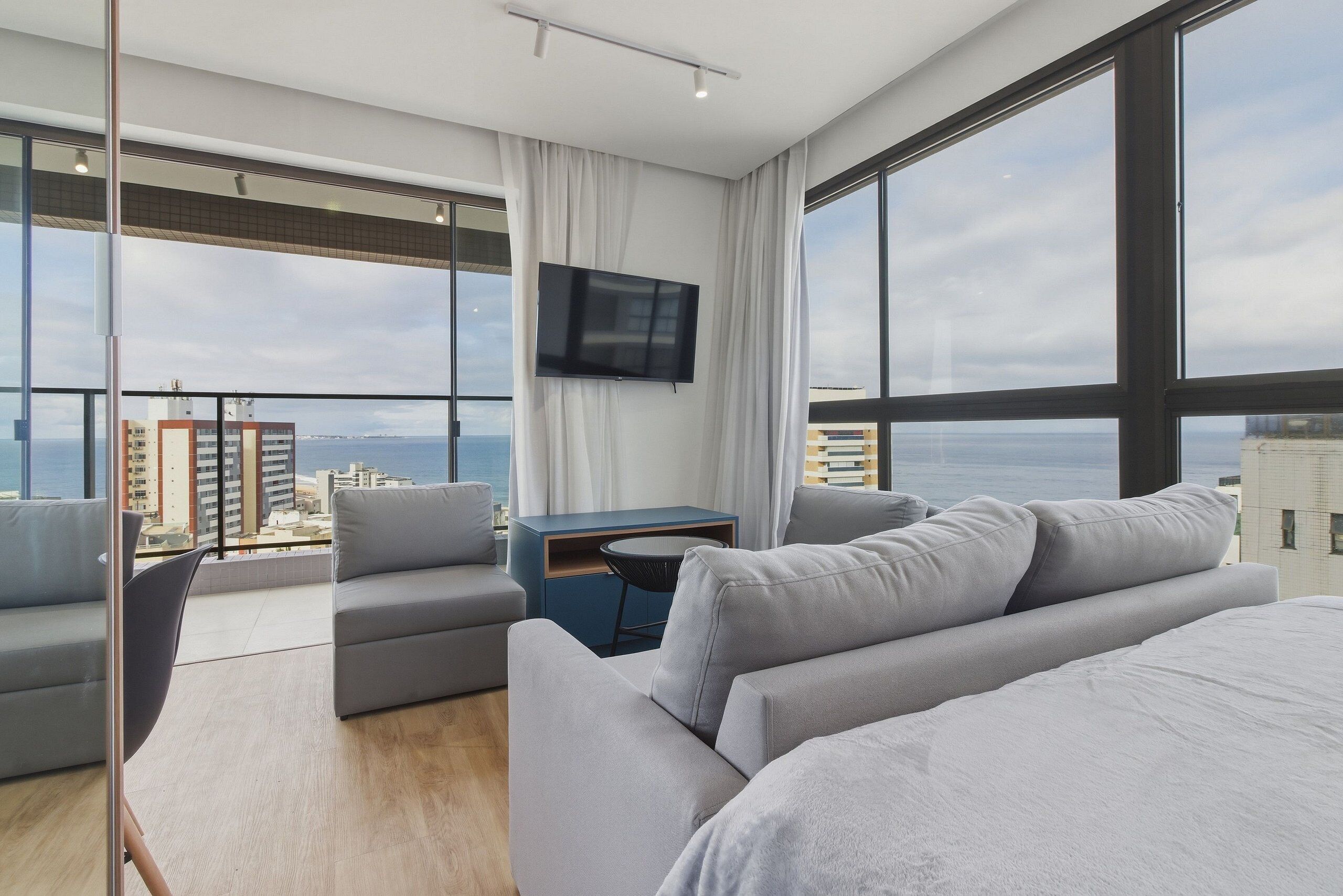 Habitación de hotel moderna con una cama grande, un sofá, un televisor y un balcón con vistas a la ciudad.