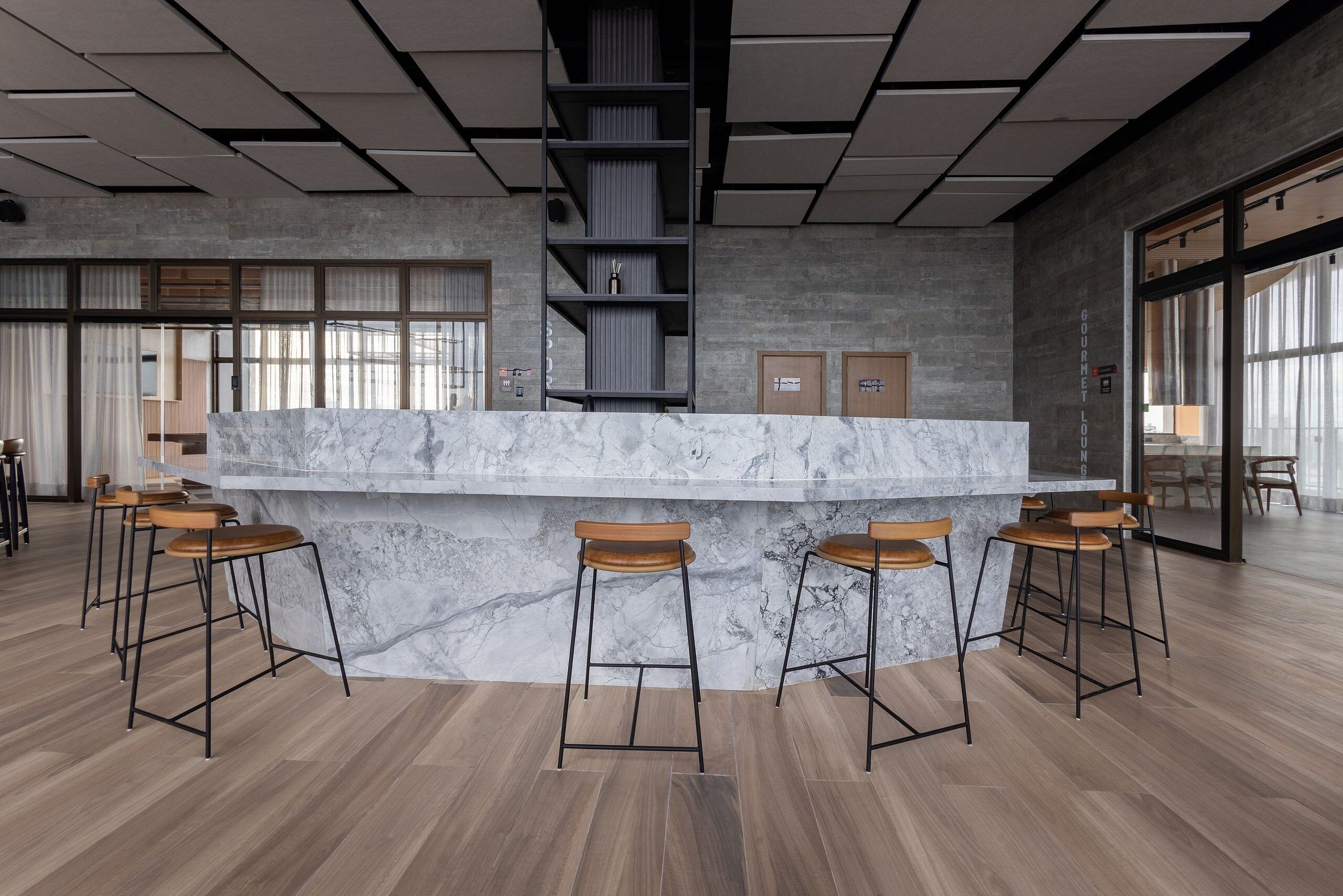 Eine moderne Bar mit einer Marmorplatte, Holzstühlen und einer hohen Decke mit freiliegenden Balken.