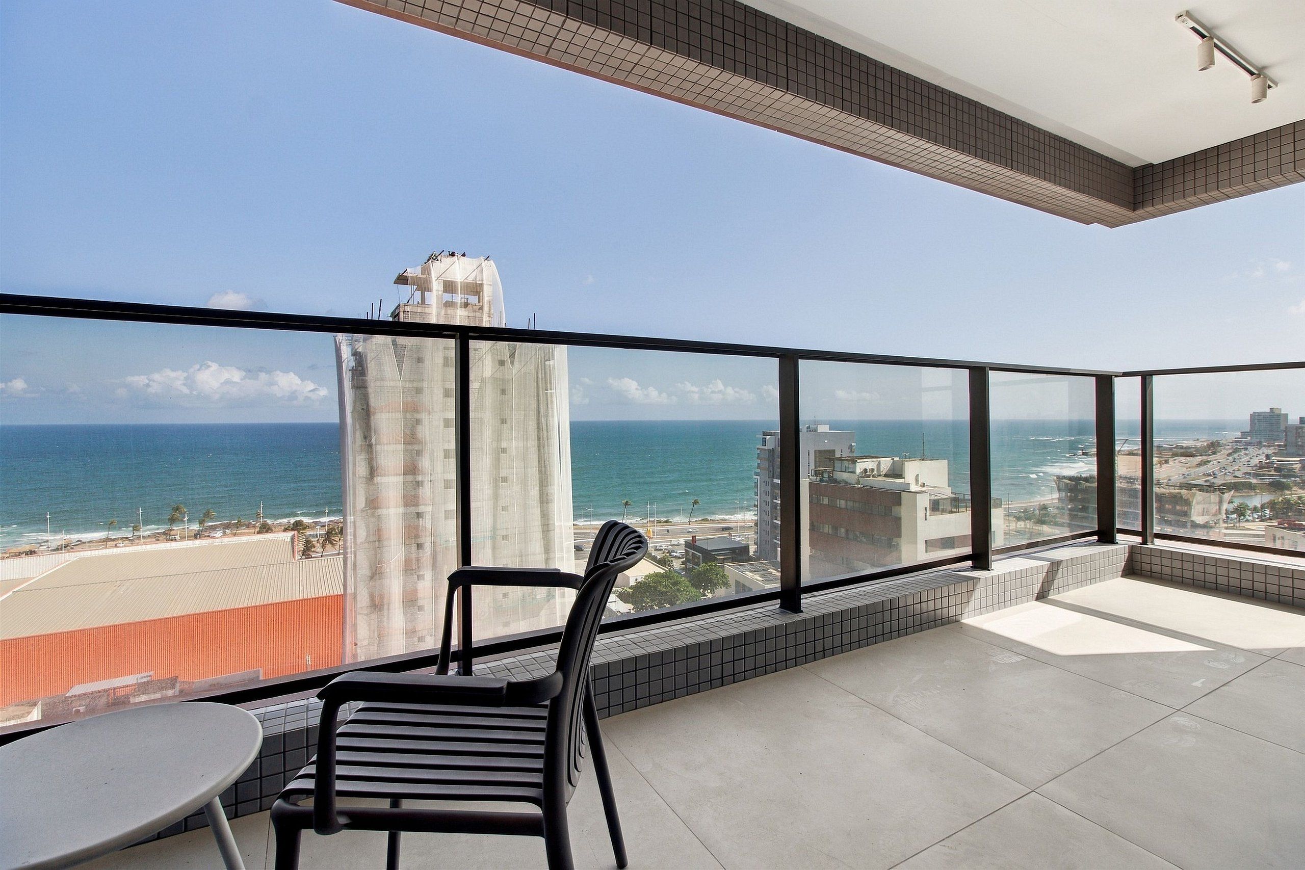 Un balcon offrant une vue sur l’océan et sur le paysage urbain, avec une chaise et une table.
