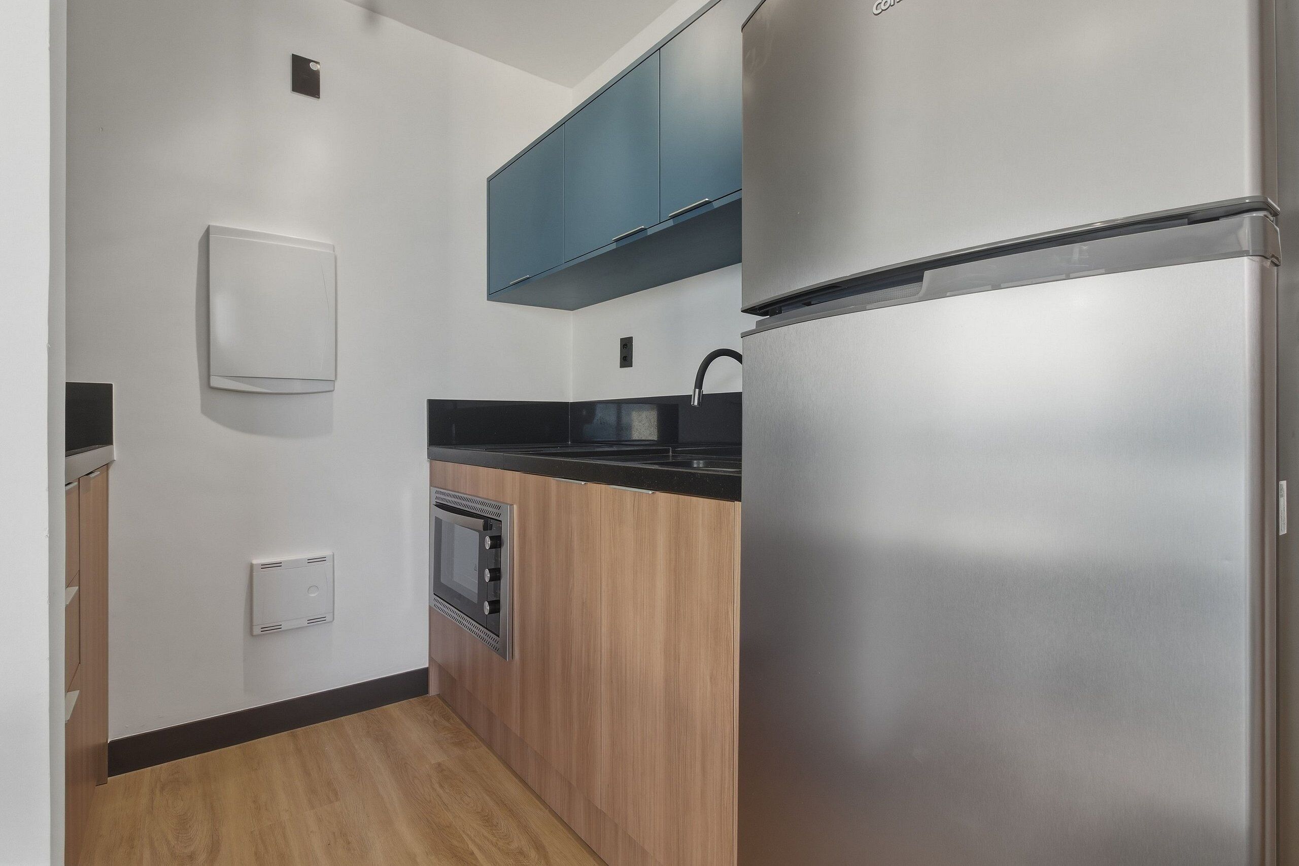 A modern kitchen with a stainless steel refrigerator, wooden cabinets, a microwave, and a black countertop.