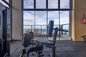 Ein Fitnessstudio mit Trainingsgeräten und Blick auf die Stadt durch große Fenster.