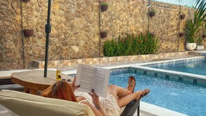A poolside area with a stone wall, lounge chairs, and a potted plant. - Horizonte del Mar Hotel Boutique  (Santa Marta)