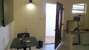 Une pièce comprenant une table à manger, des chaises, une petite plante, une paire de bottes, une porte, une fenêtre et un luminaire fixé au mur.