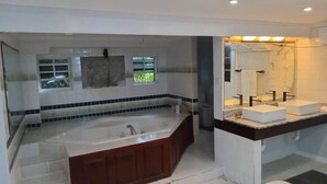 Une salle de bain moderne dotée d’une grande baignoire, d’un meuble-lavabo séparé avec un miroir et d’une fenêtre laissant entrer la lumière naturelle.