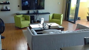 Un salon comprenant un canapé, deux fauteuils verts, une table basse, un téléviseur et une grande fenêtre.