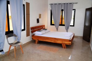 A bedroom with a wooden bed, a chair, a window with curtains, and a door.