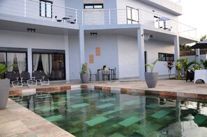 A modern building with a pool, outdoor seating, and potted plants.
