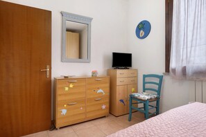 Une chambre à coucher avec une armoire en bois, un téléviseur posé sur le dessus, une chaise, un lit, un miroir et une horloge murale.