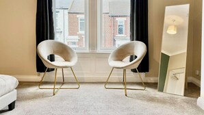 A room with two white chairs with gold legs, a white sofa, a large mirror, and a view of buildings through a window with black curtains. - South Shields Coastal House Near Beaches- South (South Shields)