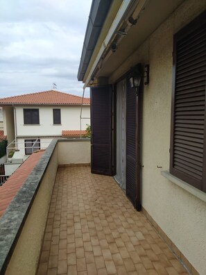 A residential balcony with a tiled floor, a closed shutter door, and a window with blinds. - Apartment 'Bilocale Buca Del Gatto 210- Cecina' with Balcony (Mazzanta)