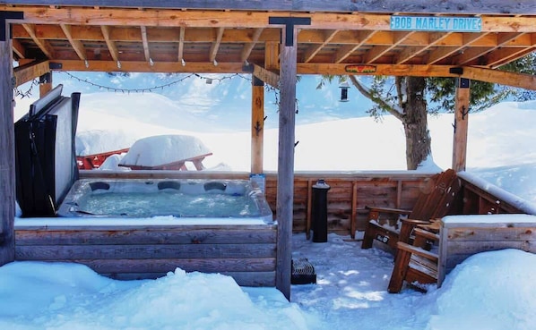 A wooden hot tub area with a wooden pergola overhead, surrounded by snow.