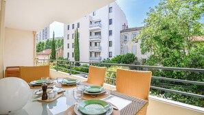 Ein Essbereich mit Tisch für vier Personen, Außenbereich und Blick auf umliegende Gebäude und Grünflächen.