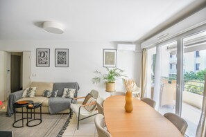 En moderne stue med sofa, spisebord, stole, en plante og billeder på væggene.