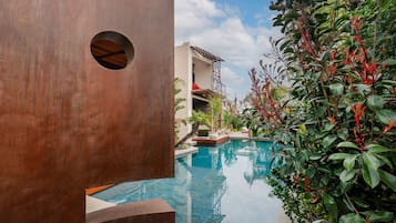 A pool area with a modern building, a circular window, and lush greenery.
