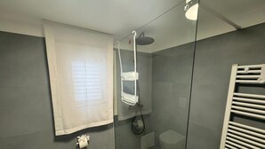 A modern bathroom with a glass shower enclosure, a white towel rack, and a patterned floor. - FRISELLA (Bari)